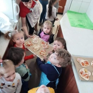 Dzieci z panią kucharką trzymają blachę z upieczonymi kawałkami pizzy