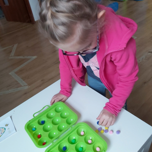 Dziewczynka układa kolorowe pomponiki wg. kodu kolorów.