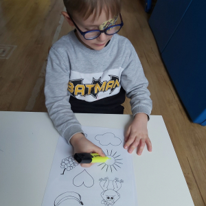 Chłopiec maluje obrazki związane z kolorem żółtym flamastrami fluorescencyjnymi.