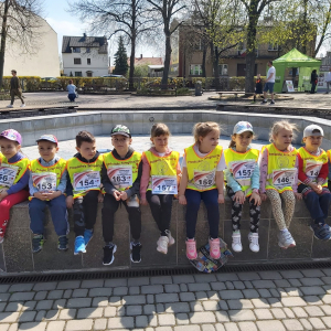 Dzieci ubrane w koszulkach reprezentujących przedszkole na biegach 3- cio majowych siedzące na murku 
