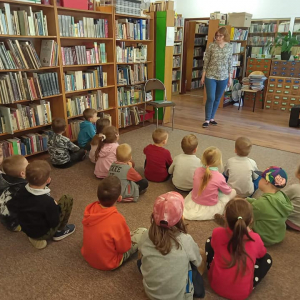 Dzieci siedzą na dywanie i słuchają pani bibliotekarki