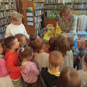 Pani bibliotekarka pokazuje dzieciom skupionym przy niej obrazki w książce 