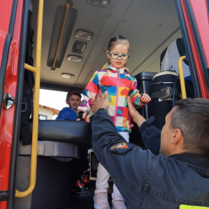 Strażak pomaga dziewczynce wysiąść z samochodu strażackiego