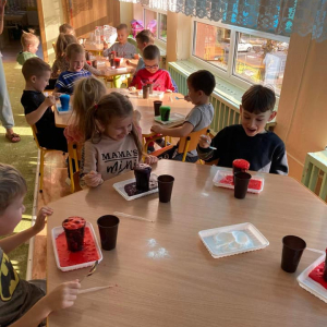 Dzieci siedzą przy stolikach i obserwują jak wypływa kolorowa woda z kubeczków