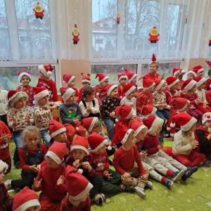 Dzieci siedzą na dywanie ubrane w czapki św. Mikołaja