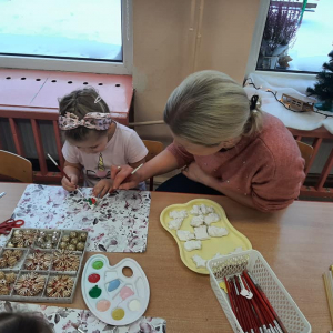 Dziewczynka z mamą maluje ozdobę choinkową