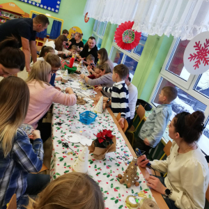 Dzieci z rodzicami siedzą przy stolikach i wykonują ozdoby świąteczne