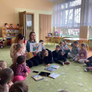 Dzieci siedzą na dywanie a Panie pokazują ilustracje do opowiadania