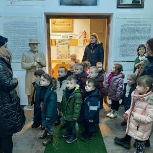 Dzieci z Paniami stoją i słuchają Pani przewodniczki Muzeum