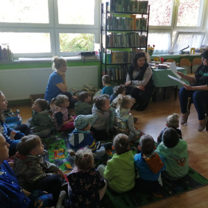 Dzieci siedzą na podłodze i słuchają czytanej bajki.