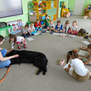 Dzieci siedzą na dywanie i kolorują obrazek psa a przed nimi leży pies
