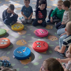 Dzieci siedzą na dywanie a przed nimi leżą poduszki z minkami