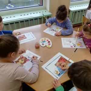 Dzieci siedzą przy stoliku i malują farbami misia