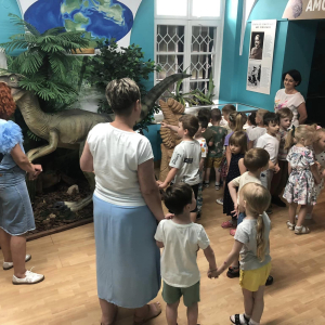 dzieci i Panie stoją i i oglądają wystawę z dinozaurami