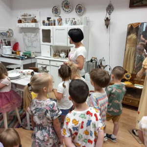 dzieci stoją i oglądają wraz z Panią wystawę z czasów PRL-u