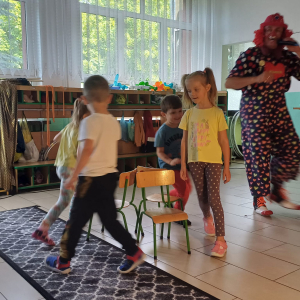 Dzieci tańczą przy krzesełkach w tle stoi klaun