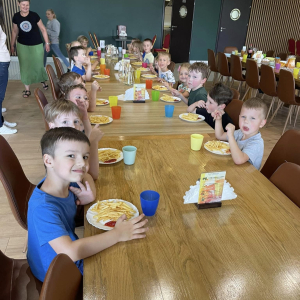 Dzieci siedzą przy stolikach i jedzą
