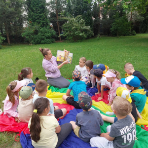 Dzieci siedzą na trawce, a pani czyta im książkę