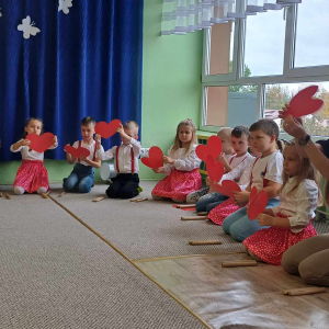 Dzieci śpiewają i machają papierowymi sercami w rytm muzyki.