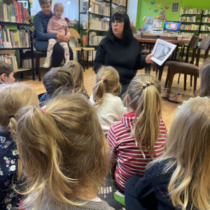 DZIECI SIEDZĄ NA DYWANIE I SŁUCHAJA PANI BIBLIOTEKARKI