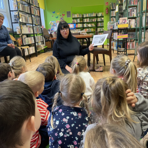 DZIECI SIEDZĄ NA DYWANIE I SŁUCHAJA PANI BIBLIOTEKARK