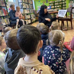 DZIECI SIEDZĄ NA DYWANIE I SŁUCHAJA PANI BIBLIOTEKARKI