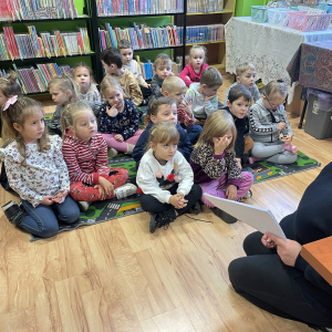 DZIECI SIEDZĄ NA DYWANIE I SŁUCHAJA PANI BIBLIOTEKARKI