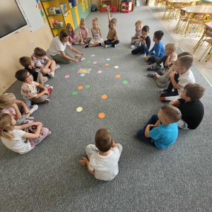 Dzieci siedzą w kole, na dywanie leżą kolorowe kropki