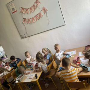 Dzieci siedzą przy stoliku i wykonują pracę plastyczną