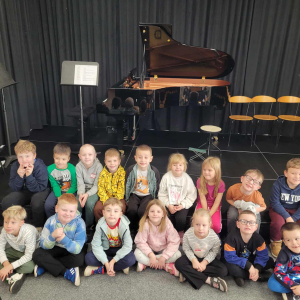 Dzieci siedzą na scenie przez fortepianem
