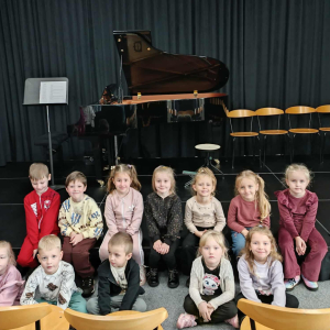 Dzieci siedzą na scenie przez fortepianem