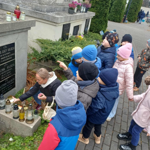 Dzieci stoja przed grobem Lotników, a pani zapala znicz.