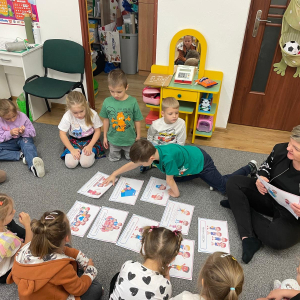 Dzieci siedzą na dywanie i słuchają nauczyciela