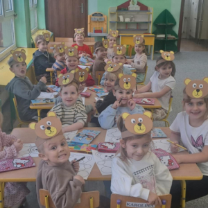 Dzieci siedzą przy stoliku i malują misia