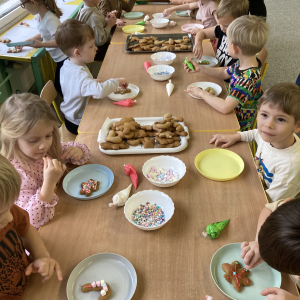 Dzieci siedzą przy stoliku i dekorują pierniki