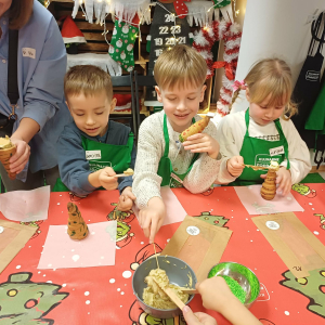 Dzieci nadziewają choinki piernikowe kremem pistacjowym.