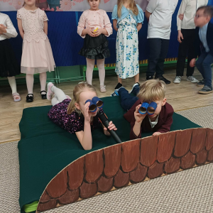 Chłopiec i dziewczynka leżą na "dachu" i patrzą przez lornetki