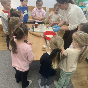 Dzieci stoją wraz z Panią i robią ciasto na pizze.