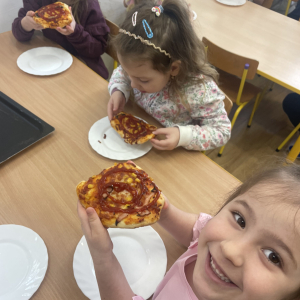 Dzieci siedzą przy stoliku i jedzą pizze.