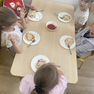 Dzieci siedzą przy stoliku i przygotowują swoje pizze.