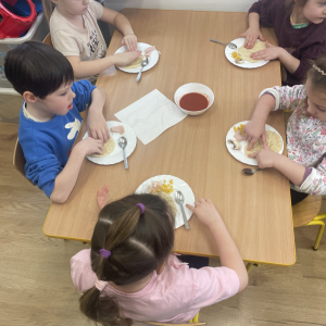 Dzieci siedzą przy stoliku i przygotowują swoje pizze.