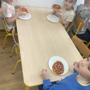 Dzieci siedzą przy stoliku i jedzą pizze.