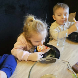 Dzieci siedzą przy stole i jedzą pizzę.