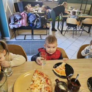 Dzieci siedzą przy stole i jedzą pizzę.