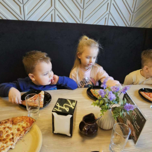 Dzieci siedzą przy stole i jedzą pizzę