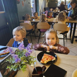 Dzieci siedzą przy stole i jedzą pizzę.