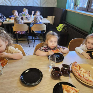 Dzieci siedzą przy stole i jedzą pizzę.