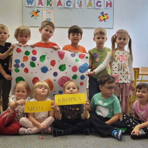 Dzieci trzymają plakat z kolorowymi kropkami. 