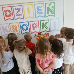 Dzieci stoją przodem do tablicy z napisem Dzień Kropki.
