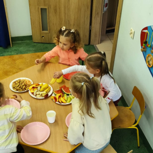 Dzieci siedzą przy stoliku i jedzą przekąski